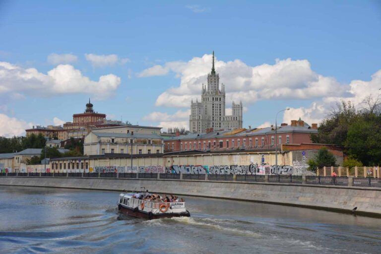 Moskau, Bild zeigt Fluss mit Boot und Gebäude im Hintergrund
